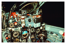 A close-up color photograph of a MiG-21 cockpit, showing a complex array of analog gauges, dials, switches, and controls on the instrument panel.